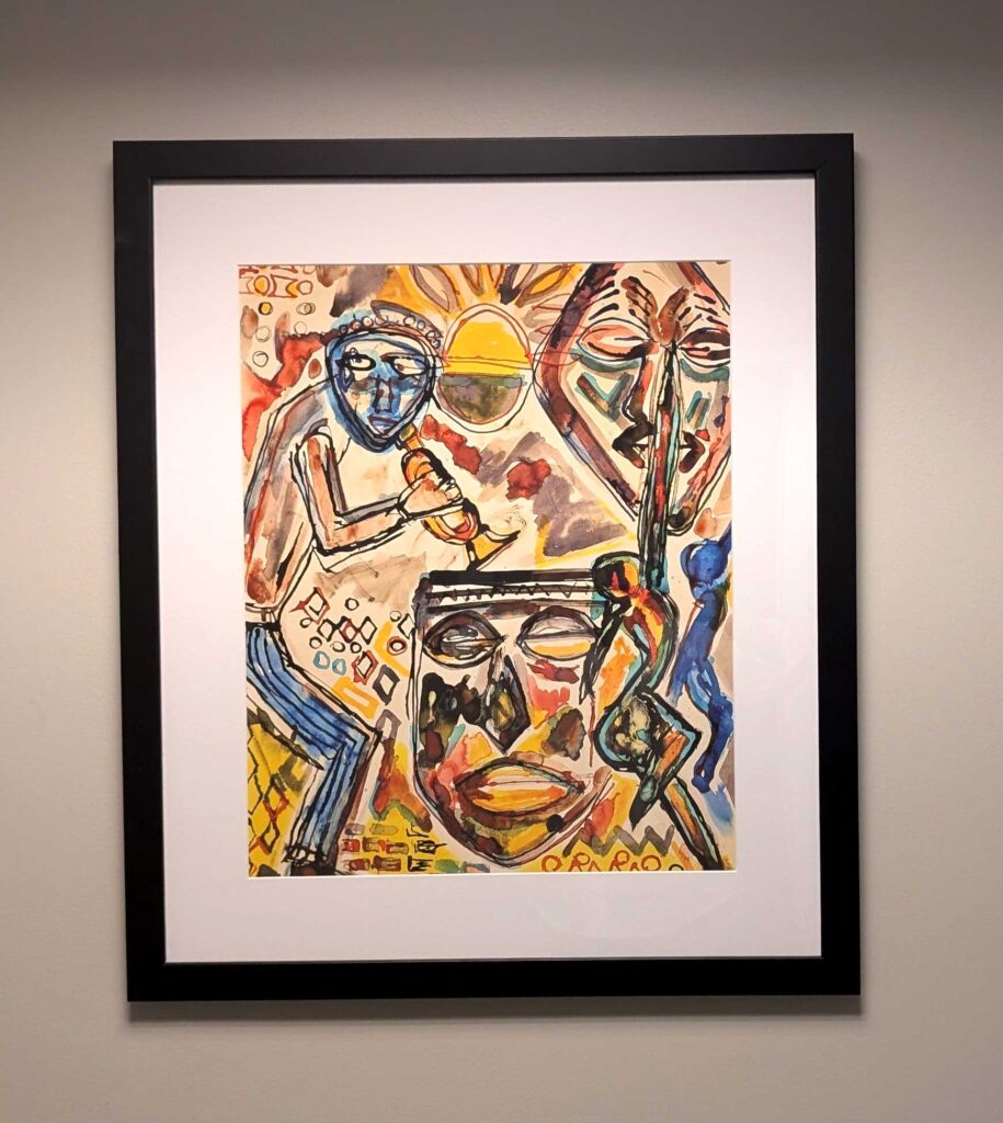 Framed abstract painting with colorful faces and figures on a light grey wall.