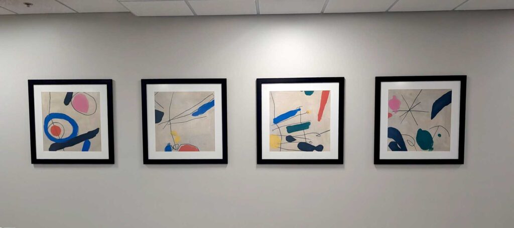 Four abstract paintings framed in black on a light-colored wall, each featuring bold shapes and colors.