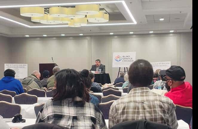 People attending a conference with a speaker at the podium in a well-lit room.